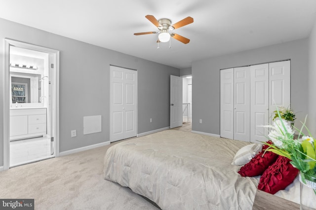 carpeted bedroom with ensuite bath, baseboards, ceiling fan, and two closets