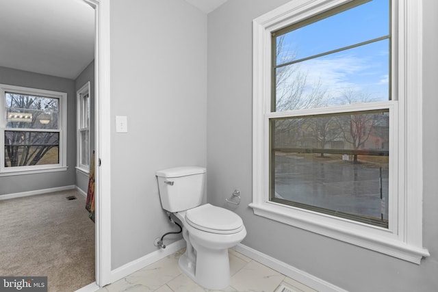 bathroom featuring toilet, marble finish floor, plenty of natural light, and baseboards