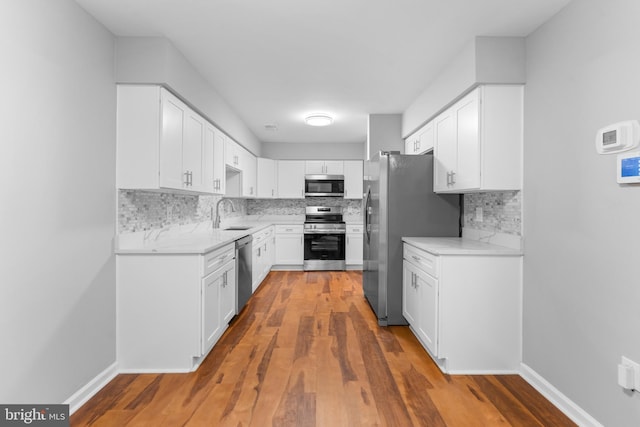 kitchen with tasteful backsplash, wood finished floors, stainless steel appliances, white cabinetry, and a sink