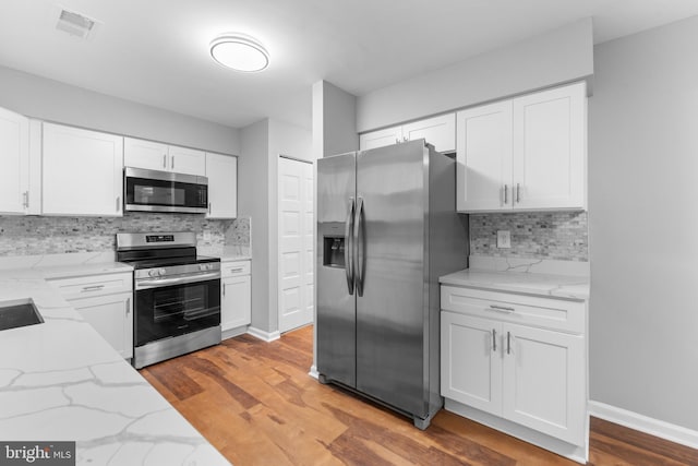 kitchen with light wood-style floors, white cabinetry, appliances with stainless steel finishes, and light stone counters