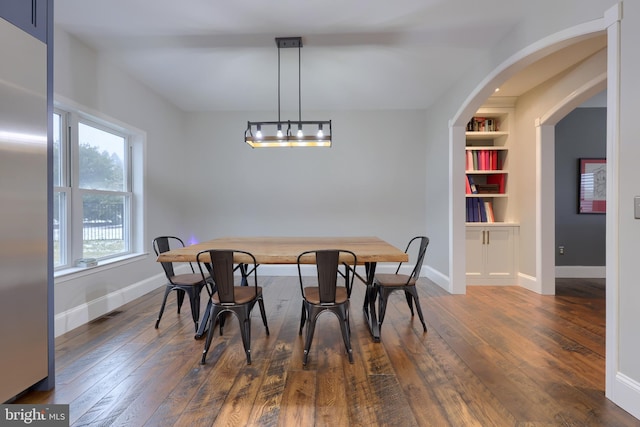 dining area featuring dark wood-type flooring, a notable chandelier, built in features, and baseboards