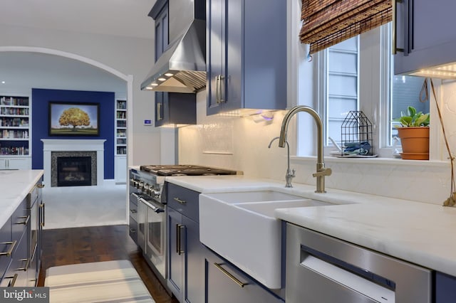 kitchen with a premium fireplace, a sink, decorative backsplash, appliances with stainless steel finishes, and wall chimney exhaust hood