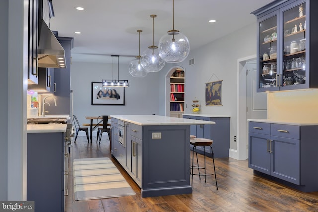 kitchen featuring a kitchen island, dark wood finished floors, recessed lighting, glass insert cabinets, and a kitchen breakfast bar