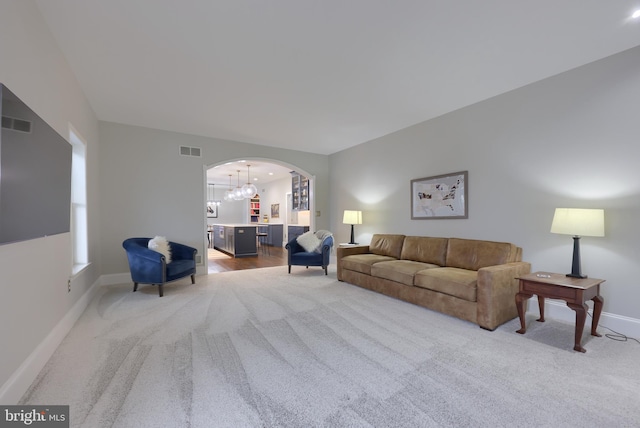 living area featuring arched walkways, visible vents, light carpet, and baseboards