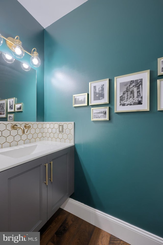 bathroom featuring baseboards, backsplash, wood finished floors, and vanity