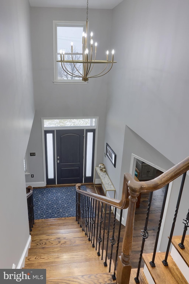 entrance foyer with baseboards, stairway, a high ceiling, wood finished floors, and a notable chandelier