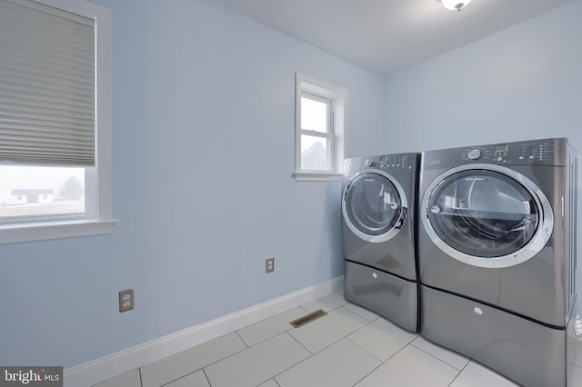 clothes washing area with visible vents, washer and dryer, light tile patterned floors, baseboards, and laundry area