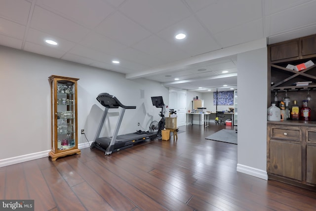 exercise area with a drop ceiling, recessed lighting, baseboards, and dark wood-style flooring