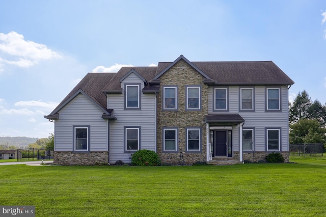 view of front of home with stone siding, roof with shingles, a front yard, and fence