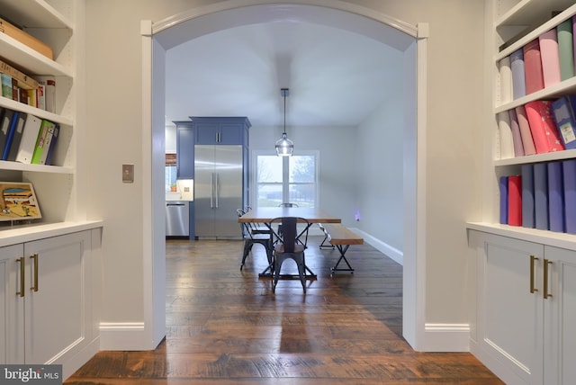 dining space featuring arched walkways, built in features, baseboards, and dark wood-style flooring