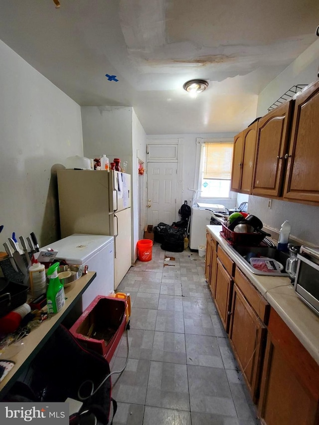 kitchen featuring a sink, brown cabinets, light countertops, and freestanding refrigerator