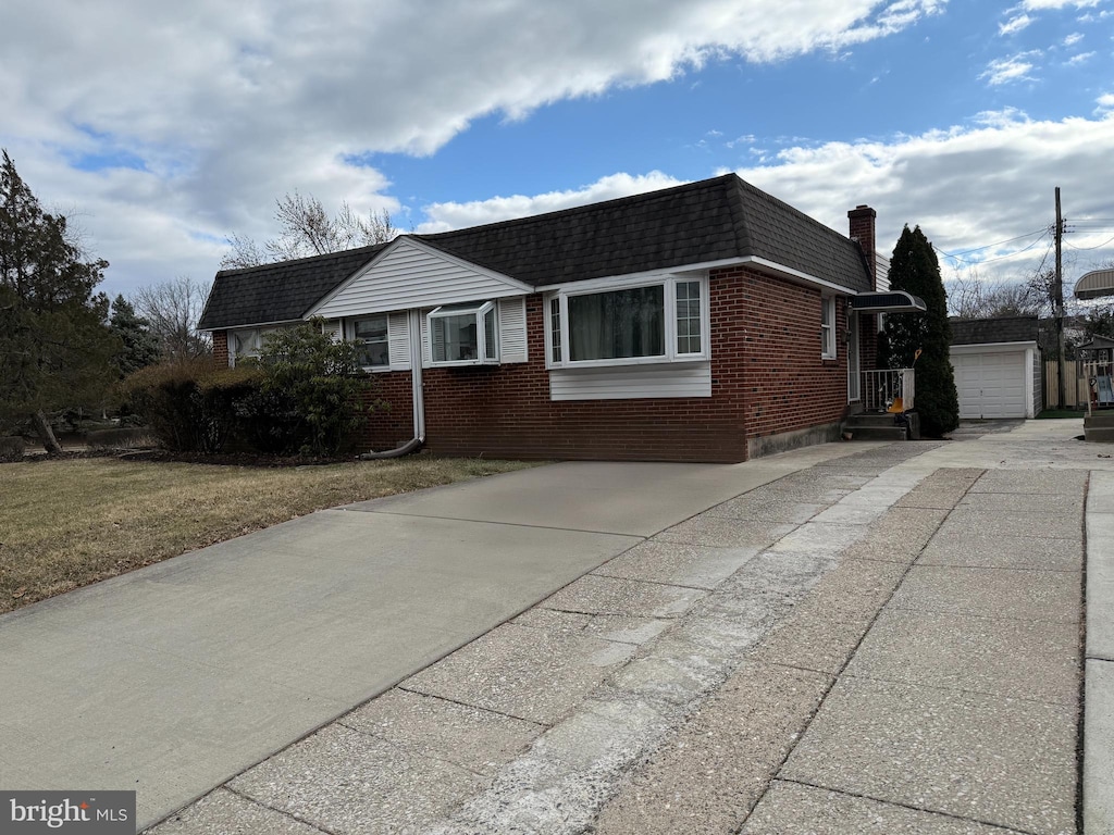 view of side of home featuring an outbuilding, mansard roof, brick siding, a shingled roof, and driveway