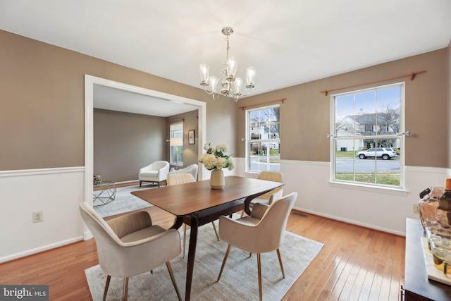 dining space with baseboards, a wainscoted wall, light wood finished floors, and an inviting chandelier