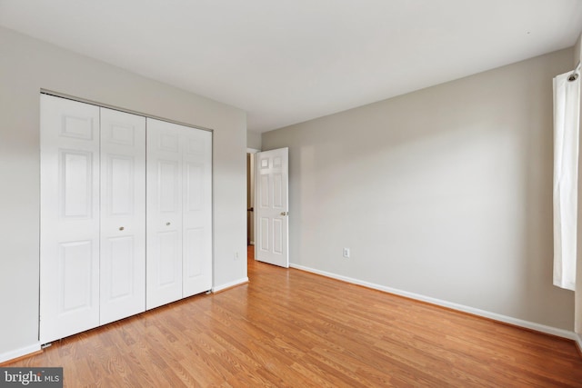 unfurnished bedroom featuring light wood-type flooring, baseboards, and a closet