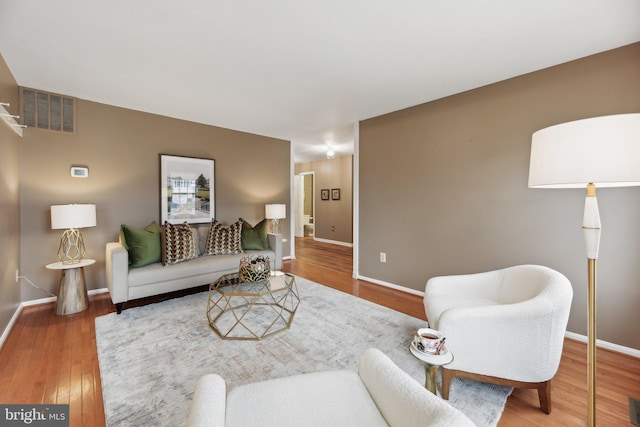 living area with wood-type flooring, visible vents, and baseboards