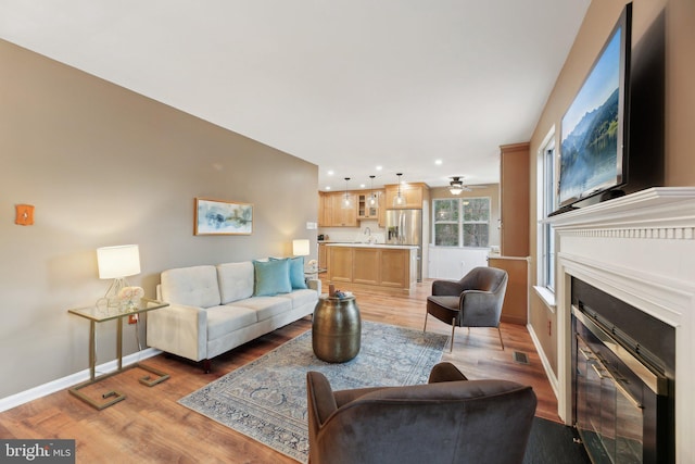 living room featuring visible vents, baseboards, a glass covered fireplace, light wood-style flooring, and recessed lighting