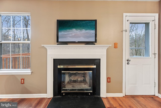 unfurnished living room with a fireplace with flush hearth, baseboards, and wood finished floors