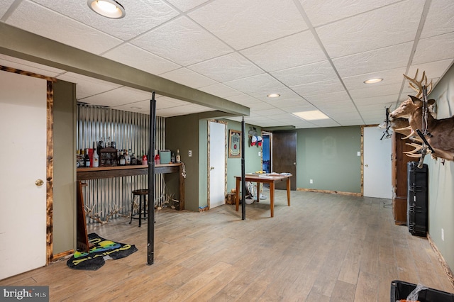 finished below grade area featuring a drop ceiling, baseboards, wood finished floors, and a dry bar