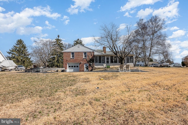 back of house with a sunroom, a chimney, a garage, a lawn, and brick siding