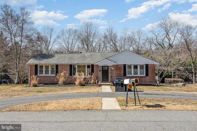 view of front facade featuring aphalt driveway, brick siding, and a front yard