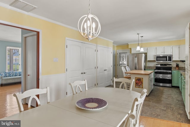 dining space featuring wood finished floors, visible vents, ornamental molding, wainscoting, and a notable chandelier
