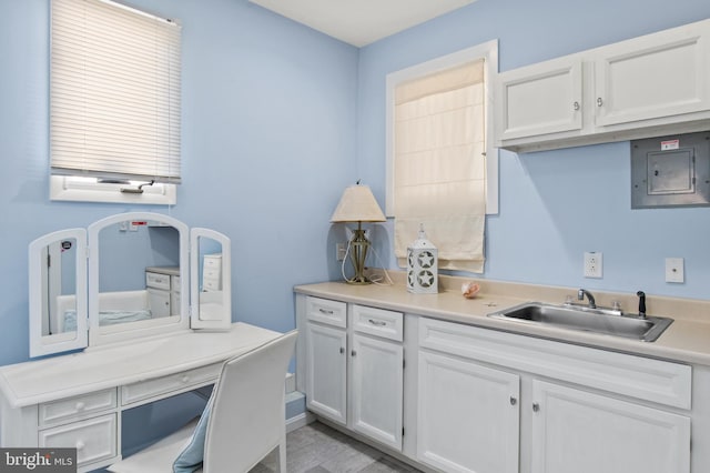 kitchen with white cabinetry, light countertops, electric panel, and a sink