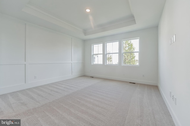 unfurnished room with light carpet, baseboards, visible vents, a raised ceiling, and a decorative wall