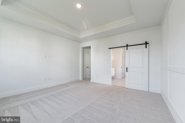 unfurnished bedroom with a barn door, recessed lighting, light colored carpet, baseboards, and a tray ceiling