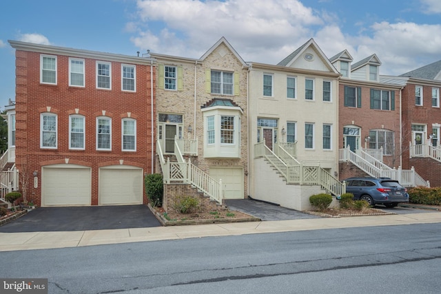 townhome / multi-family property featuring a garage, stairway, aphalt driveway, and brick siding