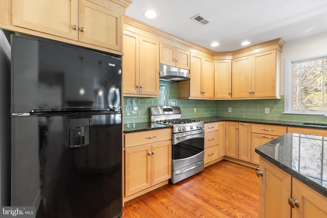 kitchen with stainless steel gas range oven, light brown cabinets, under cabinet range hood, visible vents, and freestanding refrigerator