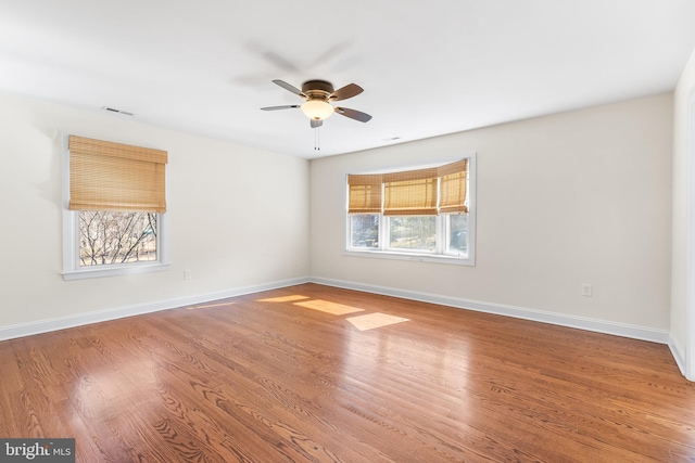 empty room featuring a ceiling fan, wood finished floors, visible vents, and baseboards