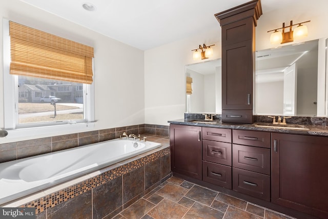 full bathroom featuring double vanity, a garden tub, stone finish flooring, and a sink