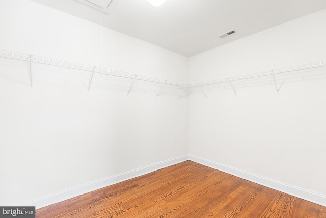 spacious closet with attic access, visible vents, and wood finished floors