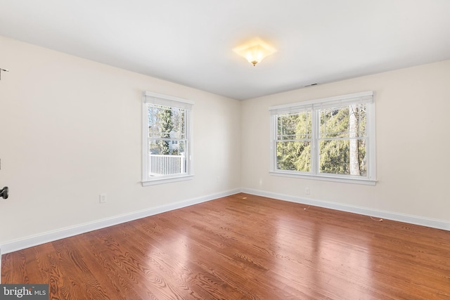 empty room featuring wood finished floors, visible vents, and baseboards