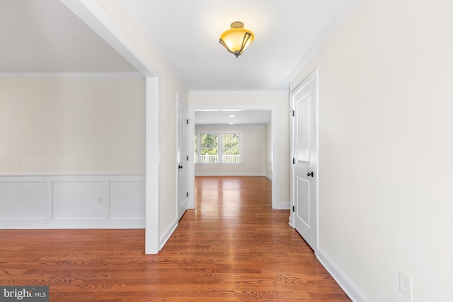 hallway with a wainscoted wall, ornamental molding, and wood finished floors