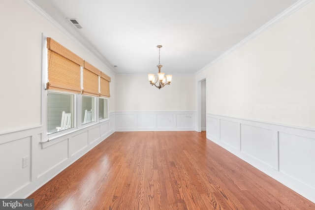 unfurnished dining area with a chandelier, a decorative wall, wood finished floors, visible vents, and crown molding