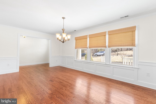 unfurnished room featuring visible vents, wood finished floors, an inviting chandelier, crown molding, and a decorative wall