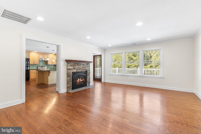 unfurnished living room with baseboards, visible vents, ornamental molding, wood finished floors, and a fireplace