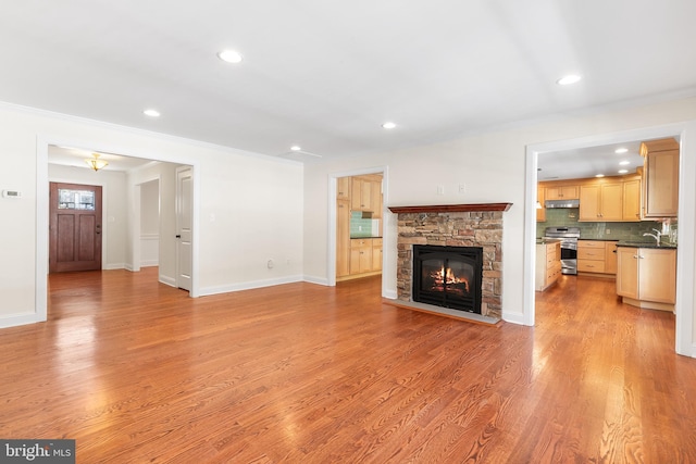 unfurnished living room with a stone fireplace, light wood-style flooring, a sink, baseboards, and ornamental molding