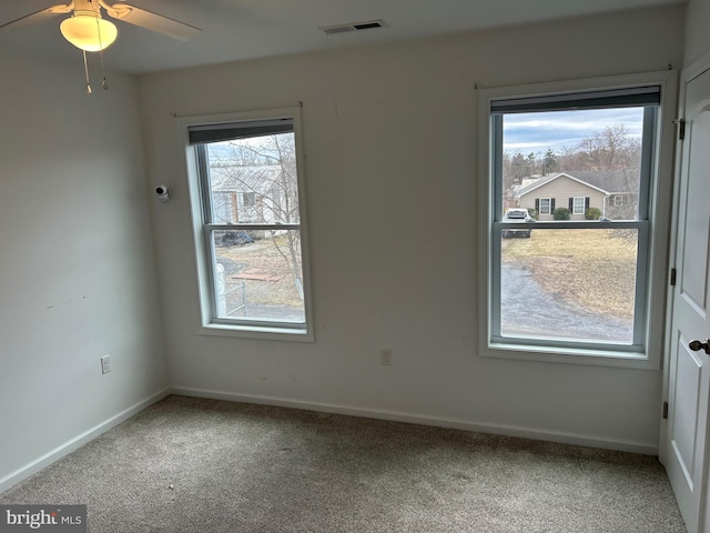 carpeted spare room with a ceiling fan, visible vents, and baseboards