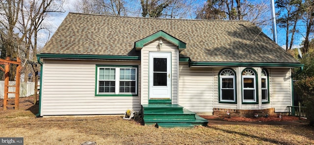 view of front of property featuring entry steps, a front lawn, and roof with shingles