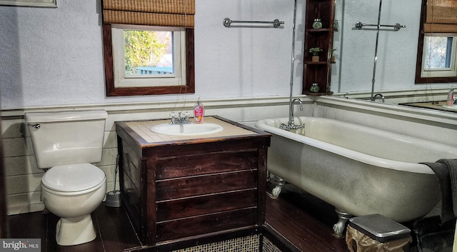 bathroom featuring a textured wall, toilet, vanity, a freestanding bath, and wainscoting