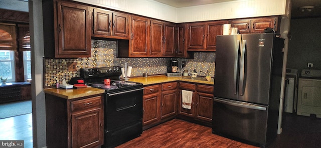 kitchen featuring tasteful backsplash, dark wood-type flooring, freestanding refrigerator, washing machine and dryer, and black / electric stove