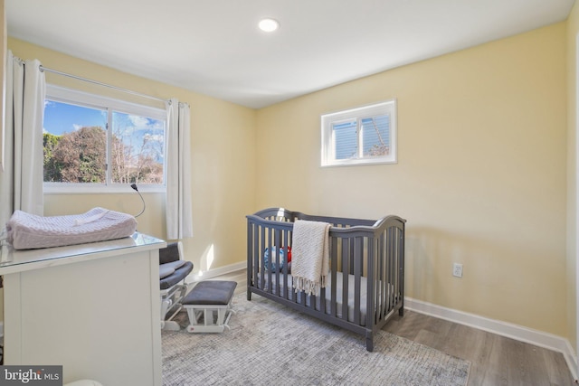 bedroom featuring a crib, recessed lighting, wood finished floors, and baseboards