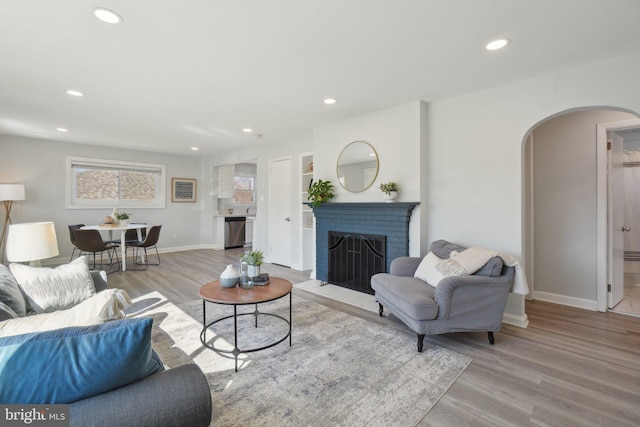 living room with a brick fireplace, recessed lighting, wood finished floors, and arched walkways