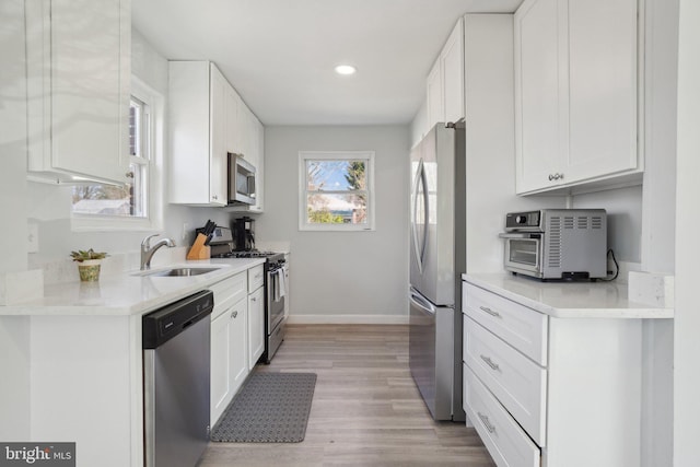 kitchen with a sink, stainless steel appliances, baseboards, and white cabinets