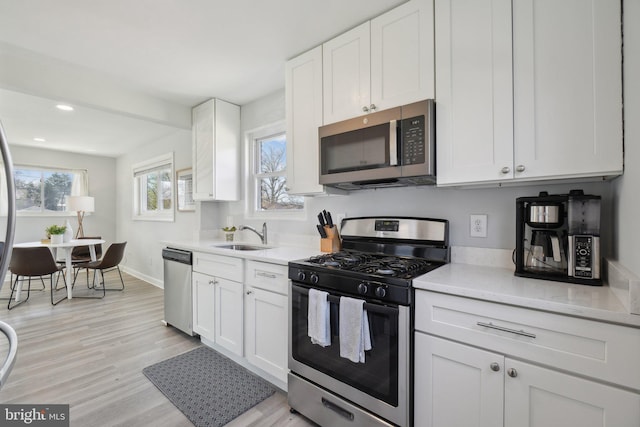 kitchen featuring a sink, light wood-style floors, appliances with stainless steel finishes, white cabinets, and baseboards