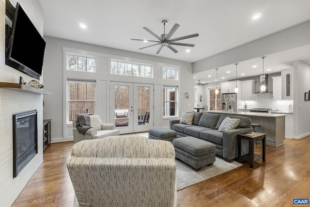 living area with french doors, a glass covered fireplace, a ceiling fan, and light wood finished floors