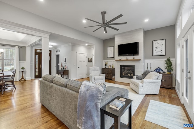 living area featuring a large fireplace, light wood-style floors, crown molding, and a decorative wall