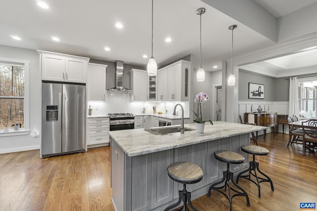 kitchen featuring a sink, light stone counters, stainless steel appliances, a breakfast bar area, and wall chimney exhaust hood